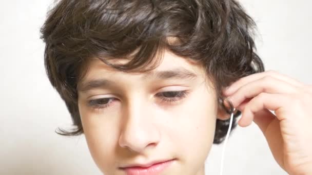 El adolescente se pone auriculares blancos y escucha música. Primer plano. espacio de copia. 4k, cámara lenta — Vídeo de stock