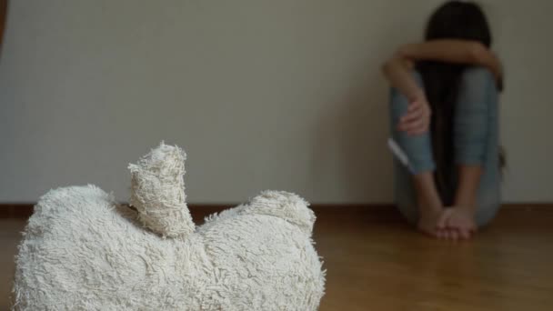 Ein verzweifeltes Kind in Depressionen sitzt an der Wand seines Zimmers und versucht Selbstmord. Daneben steht ein verlassenes Stofftier. 4k, Zeitlupe. — Stockvideo