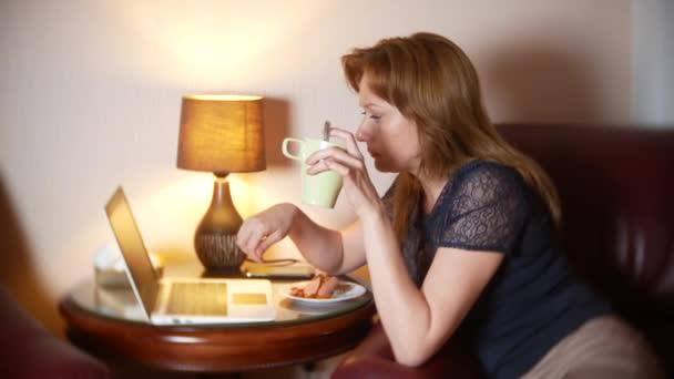 Donna che lavora di notte sul computer portatile e mangia spuntini, seduto in poltrona a casa. 4k, sfoca il bordo della cornice . — Video Stock