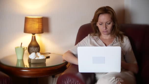 Woman working at night on laptop and eating snacks, sitting in armchair at home. 4k, blur the border of the frame. — Stock Video