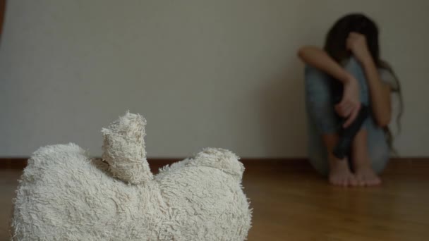 Ein verzweifeltes Kind in Depressionen sitzt an der Wand seines Zimmers und versucht Selbstmord. Daneben steht ein verlassenes Stofftier. 4k, Zeitlupe. — Stockvideo