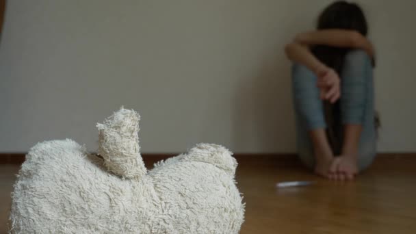 Een wanhopig kind in depressie zit op de muur van zijn kamer, probeert om te proberen van zelfmoord. ernaast is een verlaten zacht stuk speelgoed. 4k, slow-motion. — Stockvideo