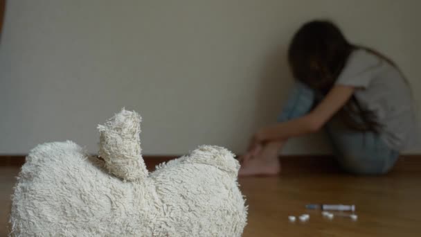 Een wanhopig kind in depressie zit op de muur van zijn kamer, probeert om te proberen van zelfmoord. ernaast is een verlaten zacht stuk speelgoed. 4k, slow-motion. — Stockvideo