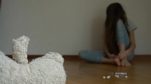 Un enfant désespéré dans la dépression est assis au mur de sa chambre, tente de se suicider. à côté se trouve un jouet mou abandonné. 4k, au ralenti . — Video