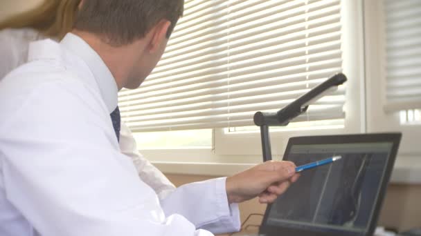 Médico olhando para a tela do computador enquanto o paciente se move na máquina de ressonância magnética, o médico analisa os resultados da ressonância magnética em seu laptop. 4k, borrão de fundo — Vídeo de Stock