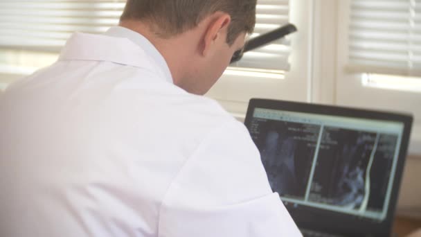 Der Arzt betrachtet den Computerbildschirm, während sich der Patient im MRI-Gerät bewegt, und analysiert die Ergebnisse der Magnetresonanztomographie auf seinem Laptop. 4k, Hintergrund verschwommen — Stockvideo