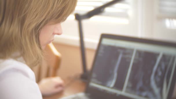 Médico olhando para a tela do computador enquanto o paciente se move na máquina de ressonância magnética, o médico analisa os resultados da ressonância magnética em seu laptop. 4k, borrão de fundo — Vídeo de Stock