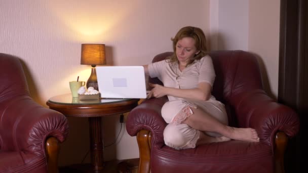 Donna che lavora di notte sul computer portatile e mangia spuntini, seduto in poltrona a casa. 4k, rallentatore . — Video Stock
