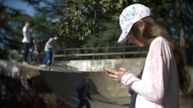 Cep telefonu açık havada kullanarak tek başına bir kız. diğer çocuklar aktif iken. Smartphone bağımlılığı. 4k, ağır çekim