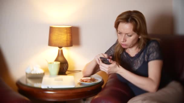 Woman uses a cellphone at night and eats snacks while sitting in a chair at home. 4k, blur the border of the frame. — Stock Video