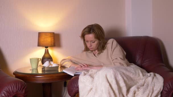 La nuit, la fille lit le livre sous une couverture sur une chaise. elle s'endort en lisant un livre ennuyeux non intéressant de 4k, au ralenti — Video