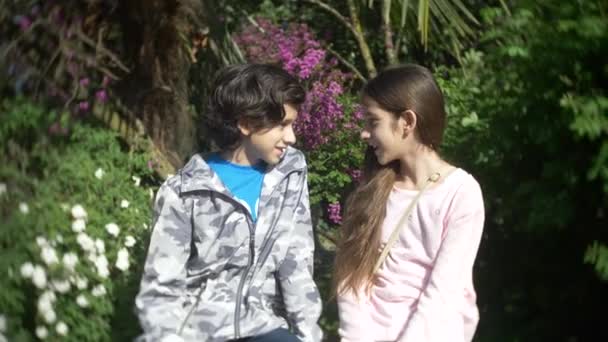 Два милих хлопчика і дівчинка розмовляють у квітучому весняному парку. 4k, повільний рух — стокове відео