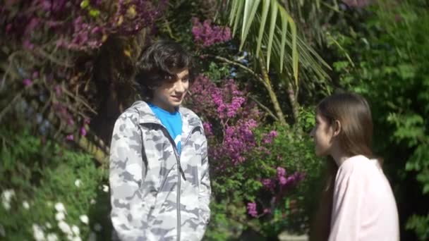 Dvě roztomilé dospívající chlapec a dívka mluví v kvetoucí na jaře parku. 4k, pomalý pohyb — Stock video