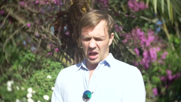 Um homem assopra seu nariz, estação da alergia, pólen, homem novo espirra no jardim da flor, 4k, câmera lenta — Vídeo de Stock