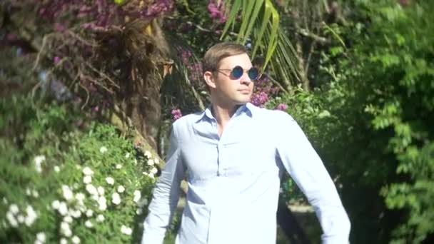 Ένας νεαρός άνδρας, φορώντας γυαλιά ηλίου σε εξωτερικούς χώρους, σε ημερήσια ηλιοφάνεια σε ένα πάρκο, 4k, αργή κίνηση — Αρχείο Βίντεο