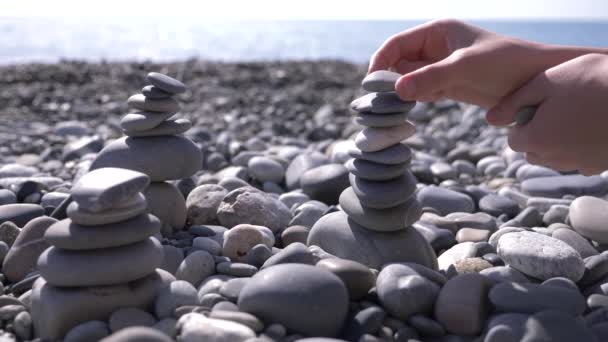 Detail, ruce složí pyramidy kameny na břehu moře. 4k, pomalý pohyb — Stock video