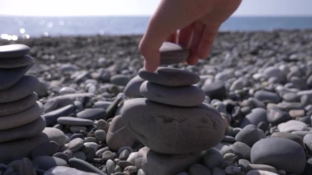 In Großaufnahme faltet die Hand eine Steinpyramide am Meeresufer. 4k, Zeitlupe — Stockvideo