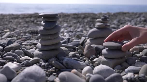 Primer plano, la mano pliega una pirámide de piedras en la orilla del mar. 4k, cámara lenta — Vídeo de stock