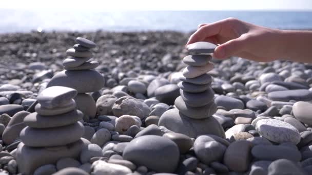 Detail, ruce složí pyramidy kameny na břehu moře. 4k, pomalý pohyb — Stock video