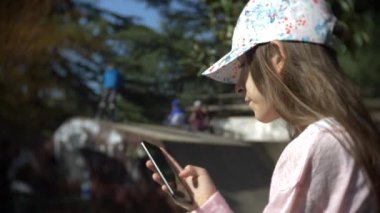 Cep telefonu açık havada kullanarak tek başına bir kız. diğer çocuklar aktif iken. Smartphone bağımlılığı. 4k, ağır çekim