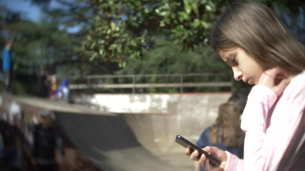 携帯電話屋外を使用して単独で女の子。他の子供たちは、アクティブな残りの部分を持っています。スマート フォン中毒。4 k、スローモーション — ストック動画