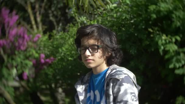 Porträt eines Jungen mit Brille, der in einem Sommerpark in die Kamera blickt. 4k. Zeitlupe — Stockvideo