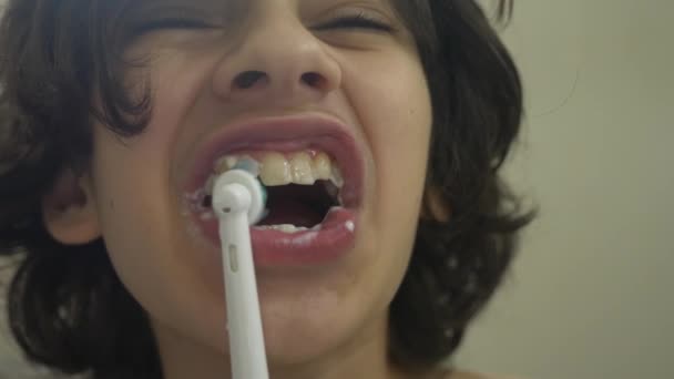 Дитина очищає зуби перед дзеркалом в 4k. хлопчик підліток щітки зуби з електричною зубною щіткою, крупним планом, повільна стрільба — стокове відео
