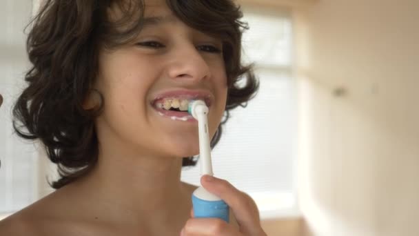 L'enfant nettoie ses dents devant un miroir en 4k. garçon adolescent brosse les dents avec une brosse à dents électrique, gros plan, tir au ralenti — Video