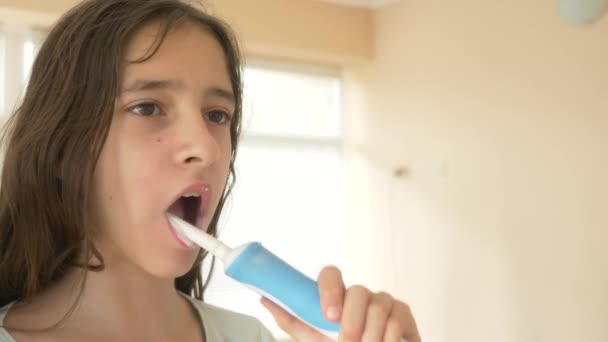 Dítě čistí zuby před zrcadlem v rozlišení 4 k. dospívající dívka čistí zuby s elektrický kartáček na zuby, close-up, zpomalené střílení — Stock video