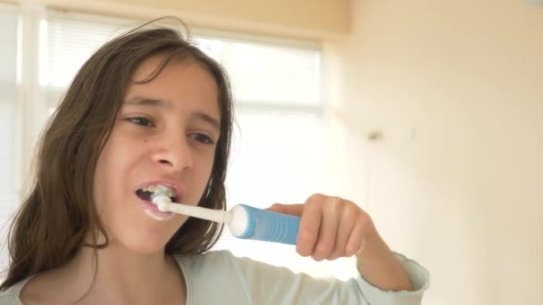 Het kind reinigt zijn tanden in een spiegel in 4 k. tiener meisje borstels tanden met elektrische tandenborstel, close-up, slow-motion-video schieten — Stockvideo