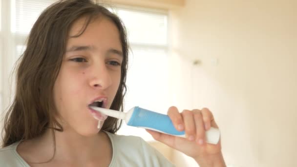 Het kind reinigt zijn tanden in een spiegel in 4 k. tiener meisje borstels tanden met elektrische tandenborstel, close-up, slow-motion-video schieten — Stockvideo