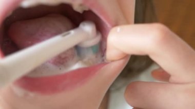 Çocuk 4 k bir ayna önünde dişlerini temizler. Kız genç elektrikli diş fırçası, yakın çekim, ağır çekim çekim ile diş fırçaları