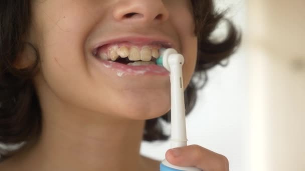 Дитина очищає зуби перед дзеркалом в 4k. хлопчик підліток щітки зуби з електричною зубною щіткою, крупним планом, повільна стрільба — стокове відео
