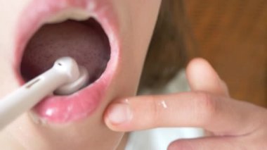 Çocuk 4 k bir ayna önünde dişlerini temizler. Kız genç elektrikli diş fırçası, yakın çekim, ağır çekim çekim ile diş fırçaları