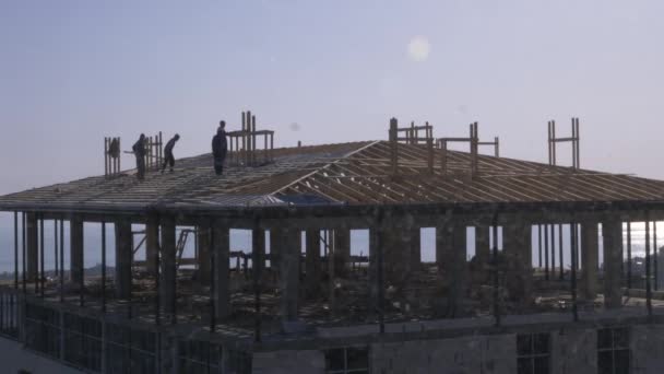 Onherkenbaar bouwers en timmerlieden werken op het dak. Een blauwe bewolkte hemel tegen de achtergrond van de zee. 4k, slow-motion — Stockvideo