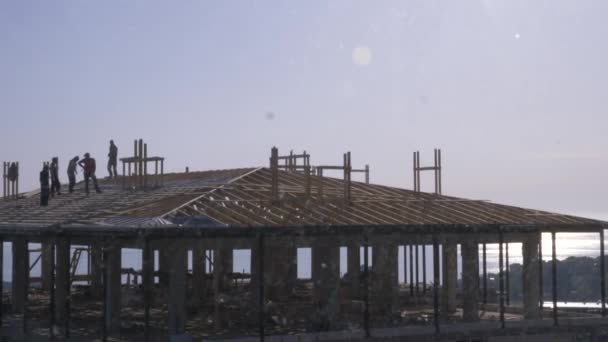 Constructores irreconocibles y carpinteros trabajando en el techo. Un cielo azul nublado sobre el fondo del mar. 4k, cámara lenta — Vídeo de stock