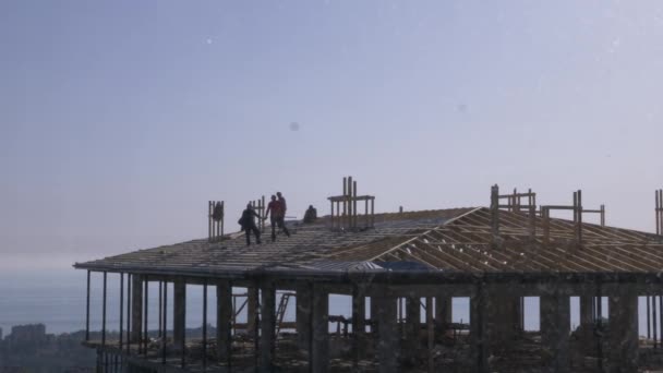 Constructores irreconocibles y carpinteros trabajando en el techo. Un cielo azul nublado sobre el fondo del mar. 4k, cámara lenta — Vídeo de stock