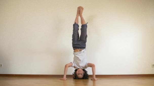 Um adolescente engraçado faz flexões de cabeça para baixo na casa. 4k, câmera lenta — Vídeo de Stock