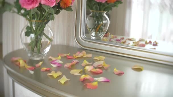 Buquê de rosas multicoloridas em um vaso de vidro redondo transparente está sobre a mesa com um espelho. 4k, câmera lenta — Vídeo de Stock
