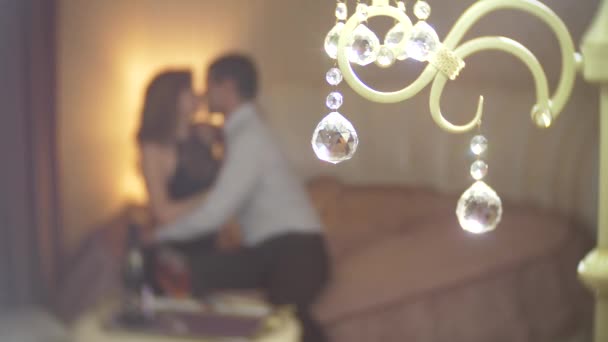 Focus on the round crystals from the lamp. Ardent loving couple is sitting on bed and hugging with passion on background. Romantic date concept. 4k, blur — Stock Video