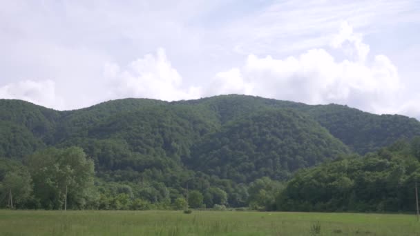 Vista desde la ventana del coche sobre un paisaje montañoso, nubes de cúmulos y árboles en un día nublado de verano. 4k, cámara lenta — Vídeo de stock