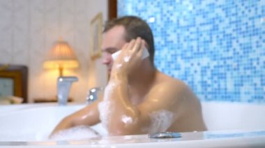 Genç bir adam banyo yaparken suya bir cep telefonu düşürür.