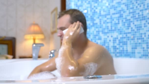 Un hombre joven deja caer un teléfono celular en el agua mientras toma un baño — Vídeos de Stock