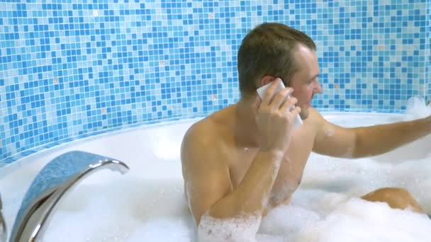 Un hombre joven deja caer un teléfono celular en el agua mientras toma un baño — Vídeo de stock