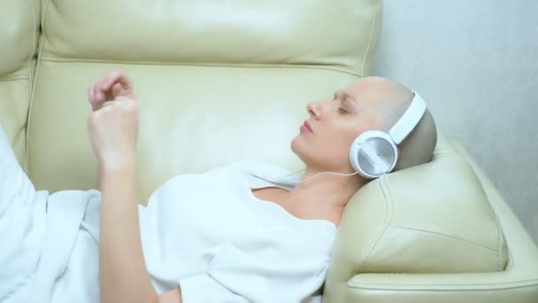 Gyönyörű kopasz lány fülhallgató élvezi a zenét otthon a kanapén — Stock videók
