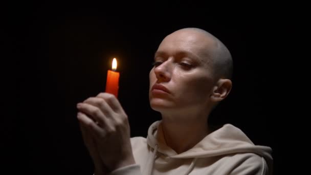 Portrait of a bald woman with a candle on a black background. copy space — Stock Video