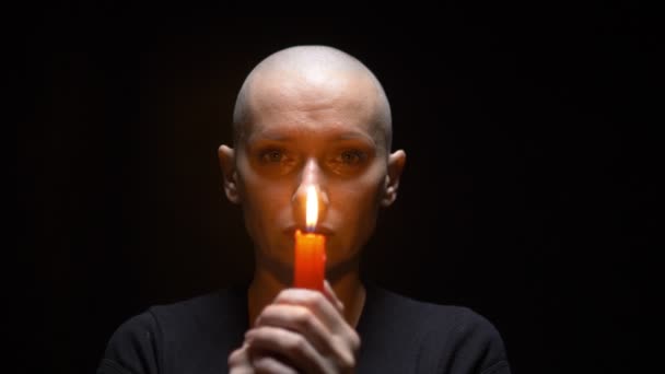 Portrait of a bald woman with a candle on a black background. copy space — Stock Video