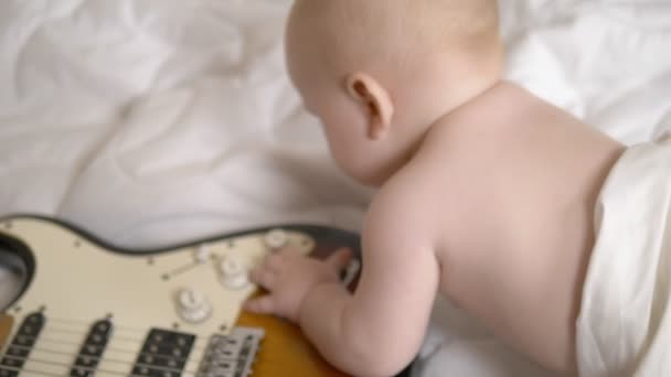 7 개월된 아기는 전기 기타를 가지고 놀고 있다. 위에서 본 광경. 어린 아이들의 음악 학교라는 개념입니다. 초기 의발 달 — 비디오