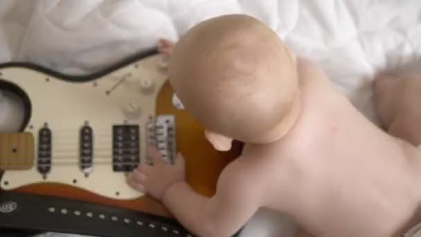 7 개월된 아기는 전기 기타를 가지고 놀고 있다. 위에서 본 광경. 어린 아이들의 음악 학교라는 개념입니다. 초기 의발 달 — 비디오