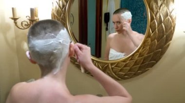 Güzel kel kadın lüks bir banyo aynasına bakar ve saçını yapar, tehlikeli bir jiletle saçını tıraş eder.